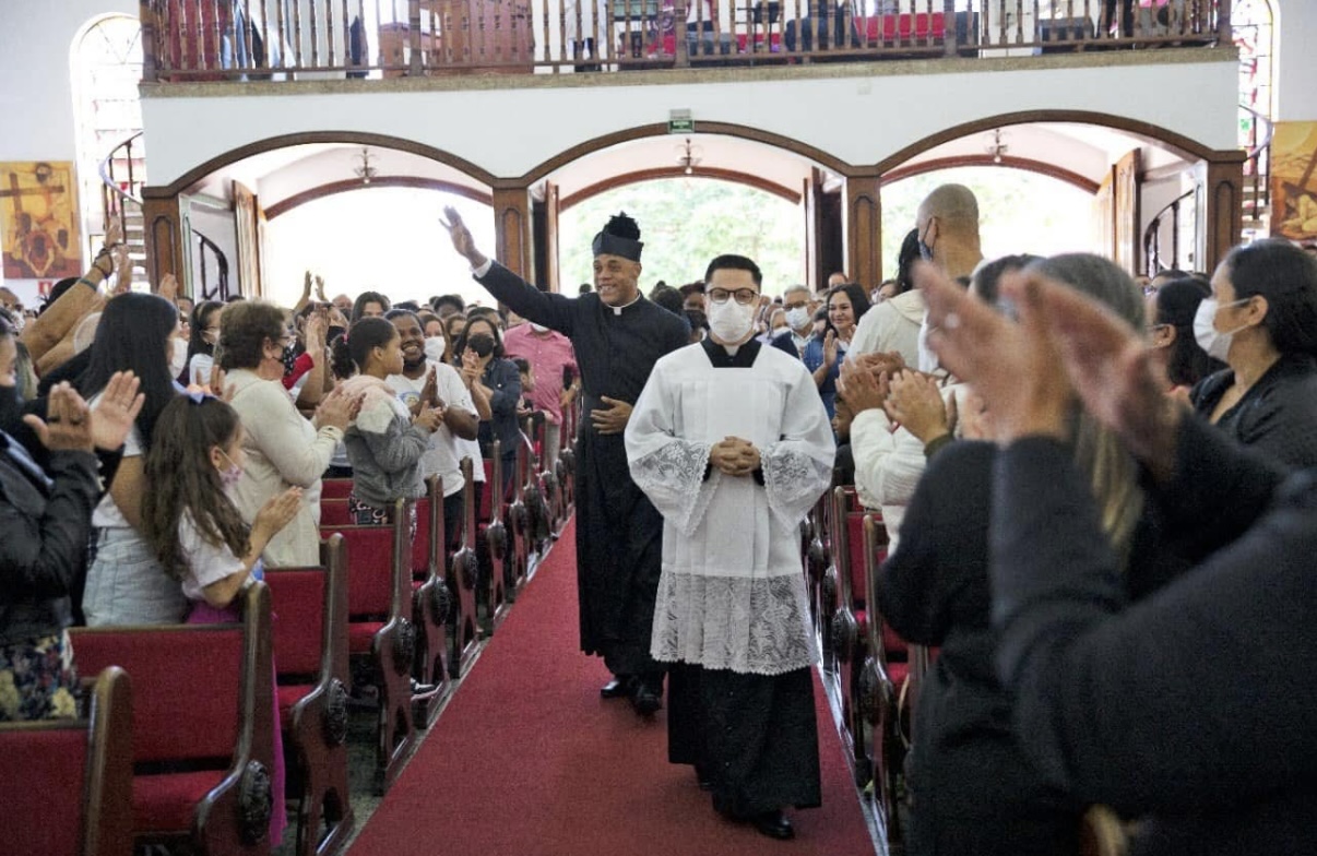 Pe. Luciano Borges Basílio entra pelo corredor central da igreja acenando, aplaudido pelos fiéis, no dia de sua posse